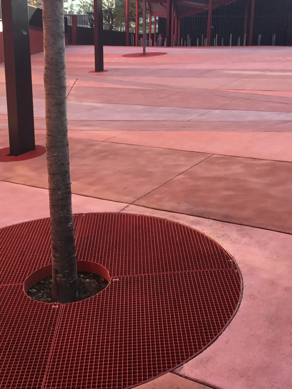 Tree grating in press-locked grating with cut-out shape and red powder coating on the renovated square of a municipality
